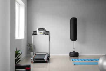 Modern treadmill and boxing pear near light wall in gym