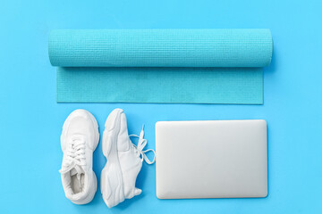 Modern laptop, sports shoes and yoga mat on color background