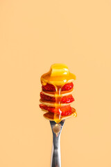 Fork with mini pancakes, fresh strawberry and piece of butter poured with honey on beige background