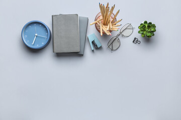 Set of stationery with eyeglasses and alarm clock on light background