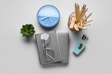 Set of stationery with eyeglasses and alarm clock on light background