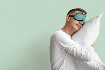 Young man with sleeping mask and pillow on green background