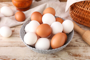 Bowl of fresh chicken eggs on light wooden background