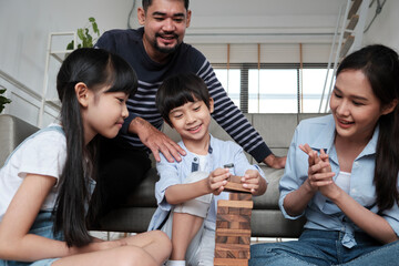 Happy Asian lovely Thai family activity, parents, dad, mum, and children have fun playing and joyful wooden toy blocks together on living room floor, leisure weekend, and domestic wellbeing lifestyle.
