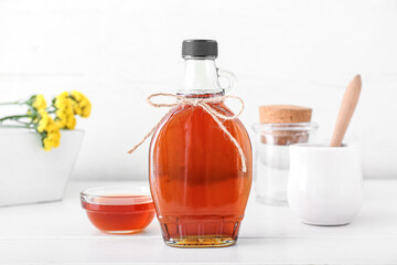 Glass bottle of maple syrup on light background