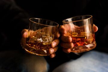 Two hands clink glasses of whiskey wiskey on the couch, cozy. Bar drinking menu.