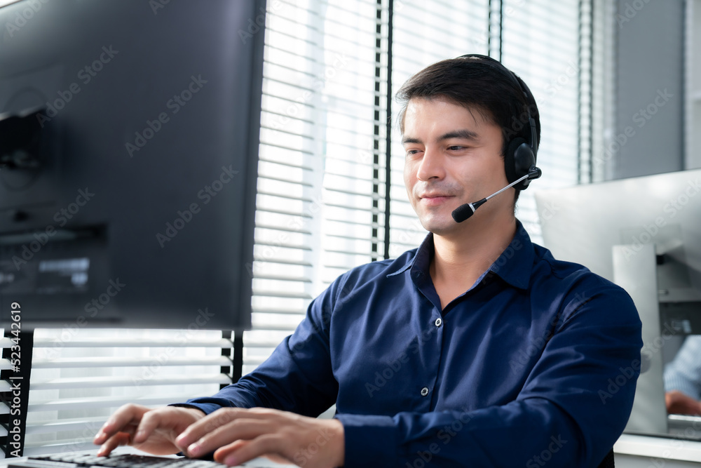 Aufkleber young competent asian male call center agent working at his computer while simultaneously speaking w
