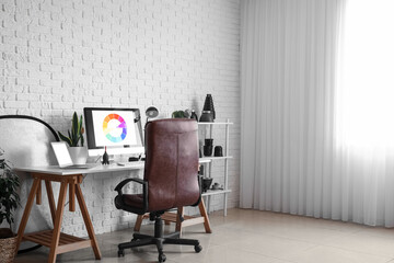 Photographer's workplace and shelving unit with equipment near white brick wall in studio