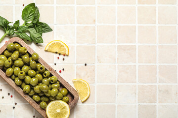 Composition with wooden board of green olives and lemon on light tile