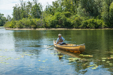 Fototapeta na wymiar A woman of retirement age solo paddles a canoe around the Toronto Islands wearing sun safe clothing in midday sun..