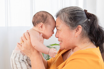 Fototapeta na wymiar Selective focus grandmother holding in air and touching foreheads with newborn baby, granny expressing understanding candid emotions and love to sweet little child. Happy friendly family concept.