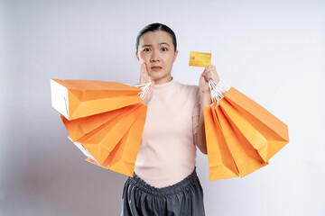 Asian woman guilty worried nervous holding more shopping bags and credit card isolated over...