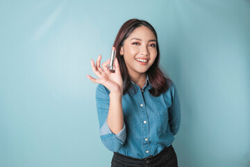 A portrait of a beautiful young Asian woman applying lipstick on her lips, isolated by a blue background