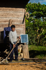 Latino man working on drying coffee, in front of his cabin with a solar panel