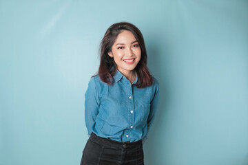Fototapeta premium A portrait of a happy Asian woman is smiling and wearing a blue shirt isolated by a blue background