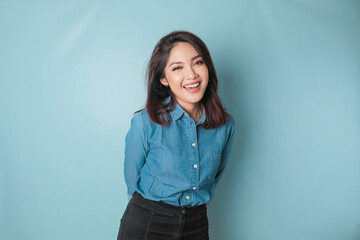 A portrait of a happy Asian woman is smiling and wearing a blue shirt isolated by a blue background