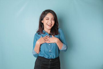 Happy mindful thankful young woman holding hands on chest smiling isolated on blue background...