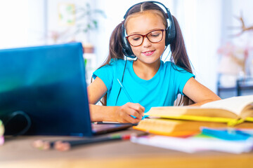 cheerful Caucasian schoolgirl wearing headphones, uses a laptop to make video calls with her teacher. child likes to study remotely. schoolgirl is happy to get knowledge. E-Education Distance Learning