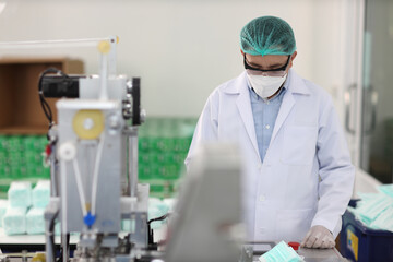Naklejka premium Worker in personal protective equipment or PPE inspecting quality of mask and medical face mask production line in factory, manufacturing industry and factory concept.
