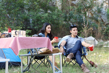 Portrait of asian couple sitting together with cup of coffee while camping in forest