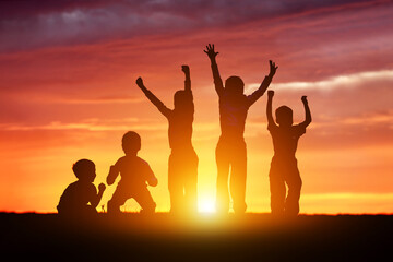 Children's happy silhouettes at sunset. Group of funny kids are jumping in the meadow on a summer evening.