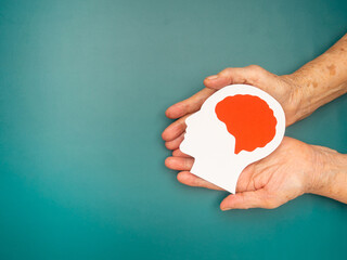 Top view of head with a brain made from paper on the palm senior woman over a green background