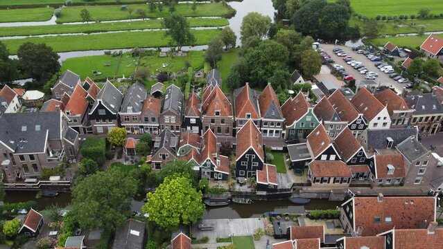 Aerial drone footage of a small Dutch village surrounded by farms and canals. Tall, narrow homes and cars line the streets and small rafts drift along the canals.