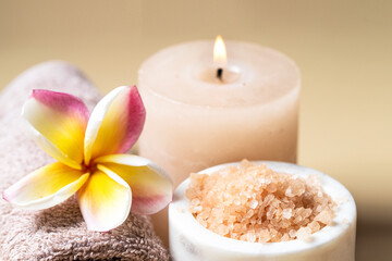 Fototapeta na wymiar Beautiful SPA composition , burning candle, towel with frangipani flowe and salt scrub on beige background . Beauty and wellness centre concept . Close up