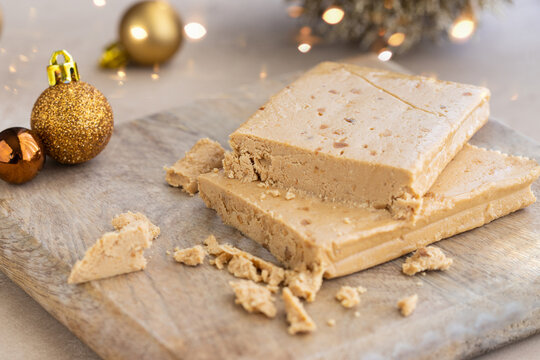 Typical Spanish Christmas sweet TURRON o almond nougat on wooden background with Christmas decoration and golden bokeh .