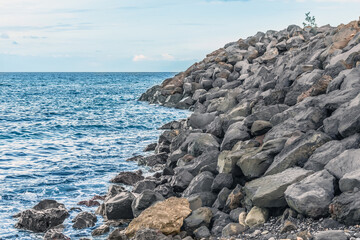 Pile of volcanic stones on the coast of the Atlantic Ocean in Santa Cruz de Tenerife in the Canary Islands, Spain. Seascape with large boulders on the shore