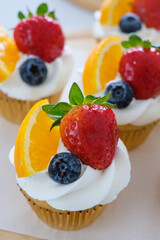 Butter cupcakes topped with strawberries, oranges and blueberries. Homemade bakery concept.