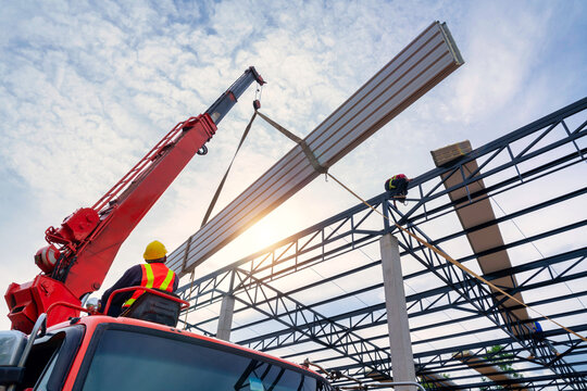 A crane driver is using a crane to lift the roof or PU foam roof sheet onto the steel roof structure at the construction site. new roof installation.