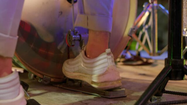 A close up image of a drummer's foot beating a drum with a pedal. White sneakers used by drummers are seen moving the bass pedal. Music video. No face video