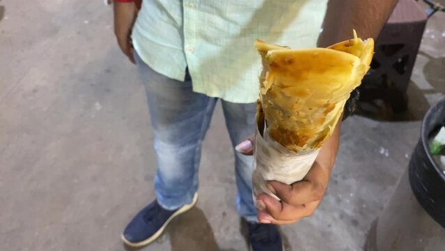 Video of a man holding a Katti roll, a popular street dish in Bengali,  where a paratha is stuffed with egg, sometimes with vegetables, chicken or mutton kabab and some condiments.