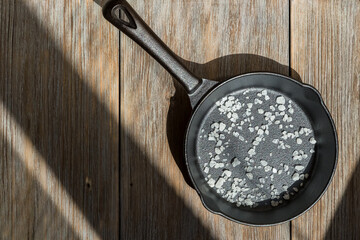 New clean cast iron pan with salt on a wooden table. Background with cooking utensils and kitchen...
