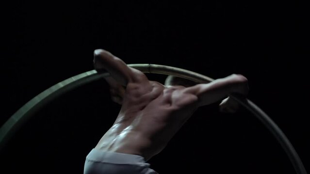 Muscular circus artist perform Cyr Wheel on a black background. Concept of willpower, motivation and healthy lifestyle