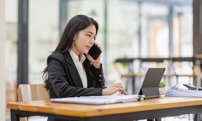 Business Asian woman talking on the phone and working with laptop calculator document on an office desk, planning analyzing the financial report, business plan investment, finance analysis concept.