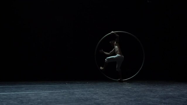 Muscular circus artist perform Cyr Wheel on a black background stage in slow motion