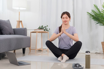 Fototapeta na wymiar Yoga exercise concept, Young Asian woman in lotus position while doing yoga exercise online at home