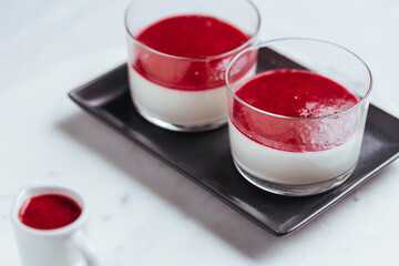 Panna cotta dessert with sauce from berries. Cherries, raspberries and blueberry as decoration. Served in two glasses on dark background. Traditional Italian creamy dessert.