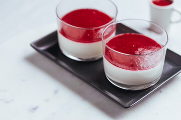 Panna cotta dessert with sauce from berries. Cherries, raspberries and blueberry as decoration. Served in two glasses on dark background. Traditional Italian creamy dessert.