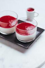 Panna cotta dessert with sauce from berries. Cherries, raspberries and blueberry as decoration. Served in two glasses on dark background. Traditional Italian creamy dessert.