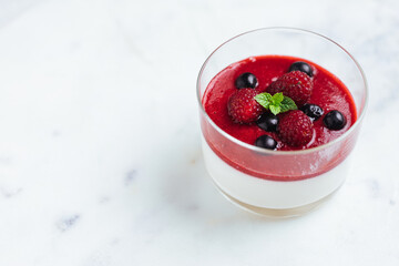 Panna cotta dessert with sauce from berries. Cherries, raspberries and blueberry as decoration. Served in two glasses on dark background. Traditional Italian creamy dessert.