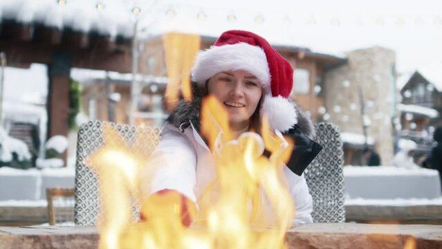 Woman in red Christmas hat roasting marshmallows in fire pit having after ski fun leisure activity at Winter holiday ski resort in Apsen. POV video of young woman grilling marshmallow stick in bonfire