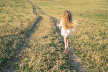 Happy childhood in the village. A child with long blonde hair runs across the field. Joyful children's games. Summer in the village at grandma's