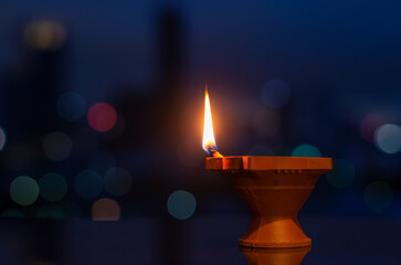 Obraz na płótnie Canvas Selective focus on flame of clay diya lamp with colorful city bokeh lights. Diwali festival concept.