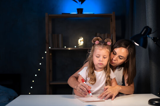 Mother teaches little preschooler to do homework by painting with color at night, image can be used for girl, study, school, mother, teacher, child, student and education