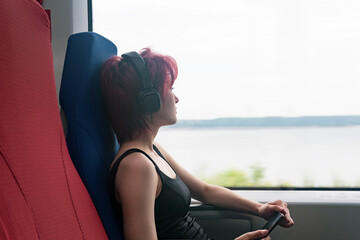 young woman rides in the train listening to music and looking out the window