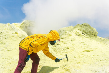 female volcanologist on the slope of a volcano next to a smoking fumarole takes a sample of a...