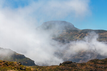Fototapeta na wymiar Clouds and fog rise against the table mountain Mesa Fortaleza de Chipude, a huge volcanic plug, Valle Gran Rey, La Gomera, Canary Islands, Spain